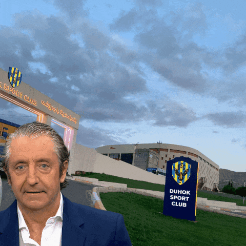 a man in a suit is standing in front of a duhok sport club sign