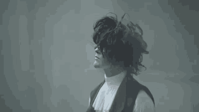 a man with long curly hair is wearing a white turtleneck and black vest .