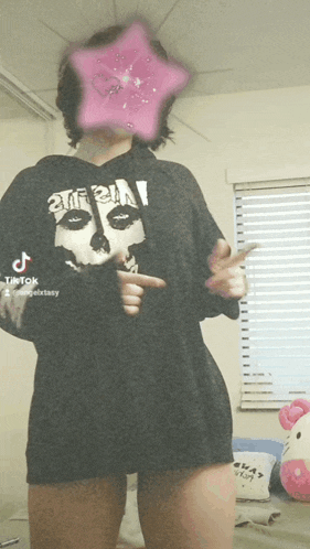 a girl wearing a black shirt with a skull on it is standing in front of a window