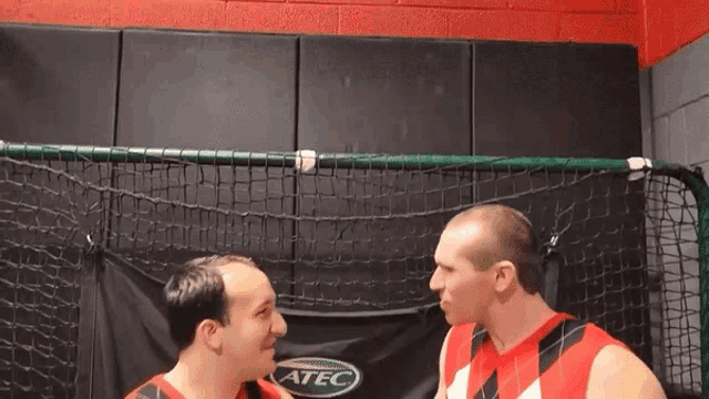 two men are facing each other in front of a soccer net that says atec