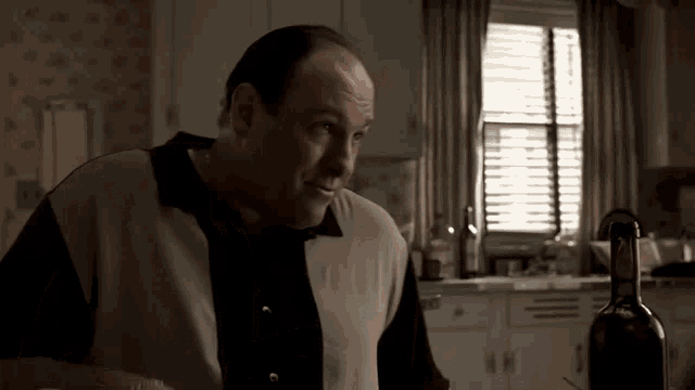 a man stands in a kitchen with a bottle of wine in front of him