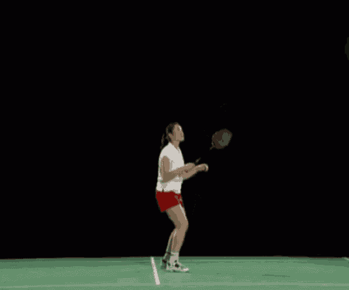 a woman in a white tank top and red shorts is swinging a tennis racket on a tennis court
