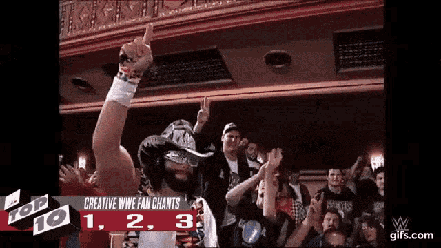 a man in a mask is giving a thumbs up in front of a crowd that is watching a wrestler