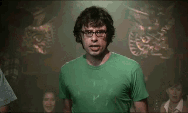 a man wearing glasses and a green shirt makes a funny face