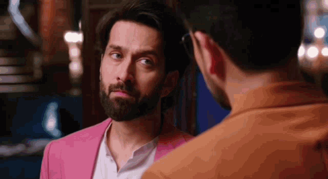 a man with a beard and a pink jacket is looking at another man .