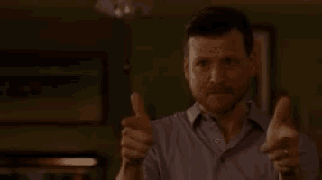 a man in a purple shirt is giving a thumbs up sign .