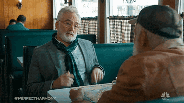 two men are sitting at a table in a diner with the nbc logo on the bottom