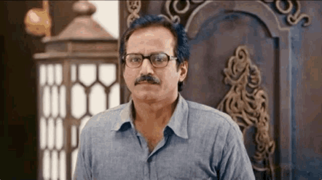 a man with glasses and a mustache is standing in front of a clock .