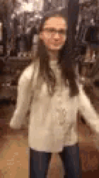 a young girl wearing glasses and a white sweater is standing in a room with her arms outstretched .