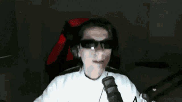 a man wearing sunglasses and headphones is sitting in a chair with a microphone .