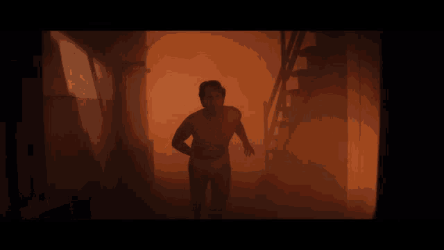 a shirtless man is running in a dark room
