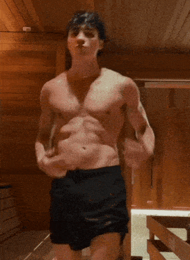 a shirtless man in black shorts is standing in a sauna