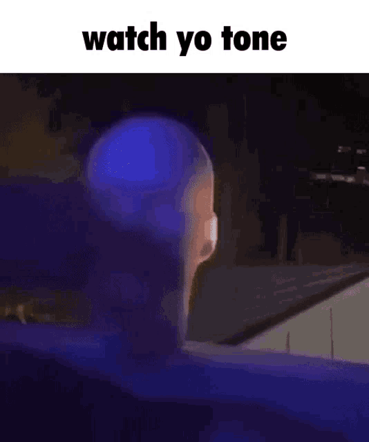 a person is standing in front of a building with a blue light coming out of it and the words `` watch yo tone '' .