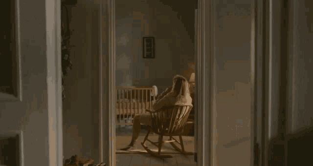 a woman is sitting in a rocking chair in a room with a crib .