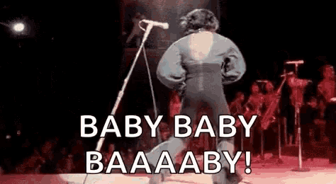 a man is dancing on a stage in front of a microphone and says `` baby baby baaaby '' .