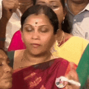 a woman in a red saree is sitting in a crowd of people