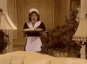 a woman dressed as a maid is holding a tray in a living room .