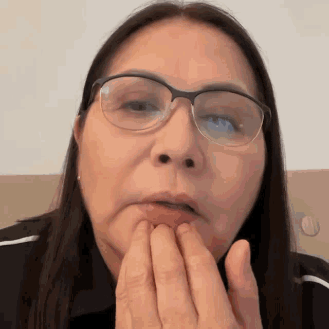 a woman wearing glasses is making a funny face while covering her mouth with her hands .