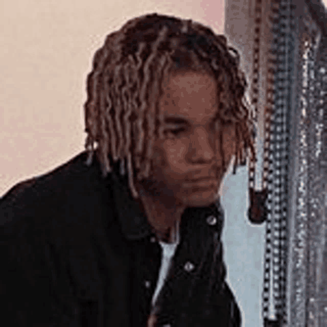 a young man with dreadlocks is standing in front of a mirror and looking at himself .
