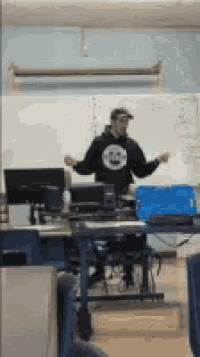 a man in a hoodie with a smiley face on it is standing in a classroom