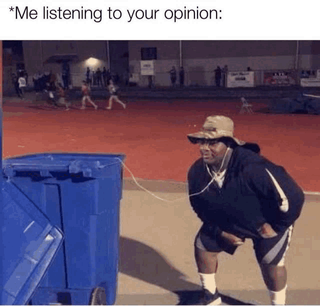 a man wearing headphones is listening to his opinion while standing next to a trash can .