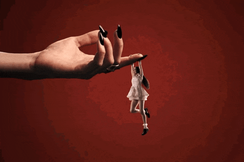 a woman 's hand with black nails is holding a small woman in a white dress