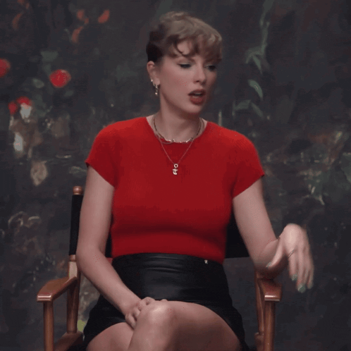 a woman wearing a red top and a black skirt sits in a chair