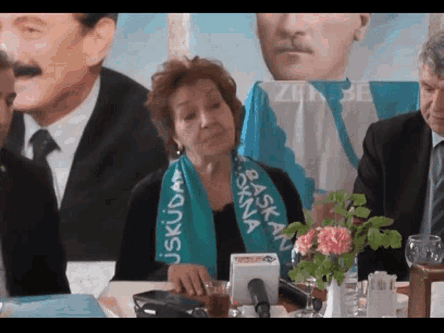 a woman wearing a green scarf that says baska on it sits at a table