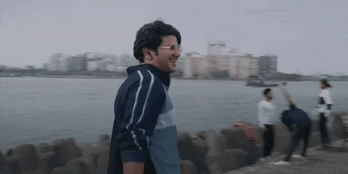 a man wearing glasses is smiling while walking along a shoreline .