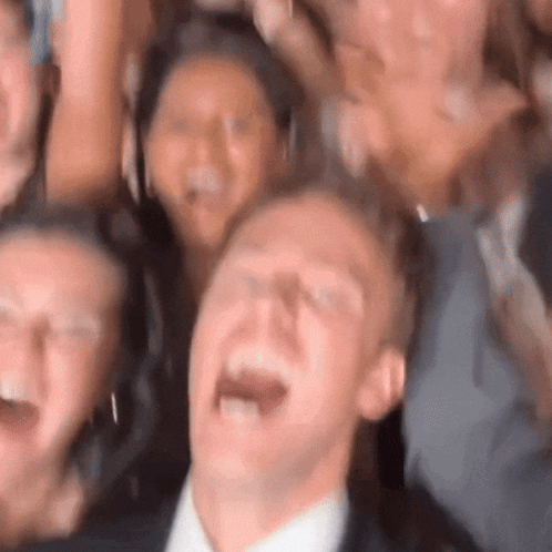 a man in a suit is laughing in front of a crowd