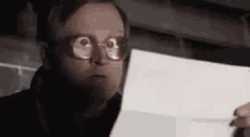 a man with glasses is holding a piece of paper in his hand .