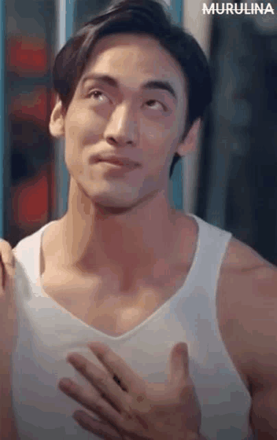 a man in a white tank top is making a funny face while holding his hands to his chest .