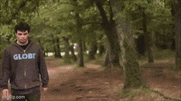 two men are standing next to each other in the woods and one of them is wearing a globe sweatshirt .