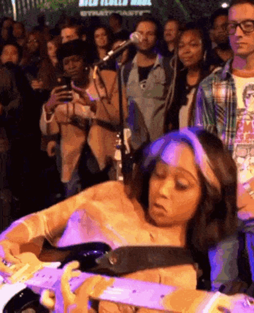 a woman is playing a guitar in front of a crowd at a concert while a man takes a picture of her ..