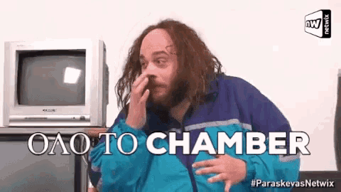 a man with long hair and a beard is covering his nose and says " olo to chamber " in front of a television