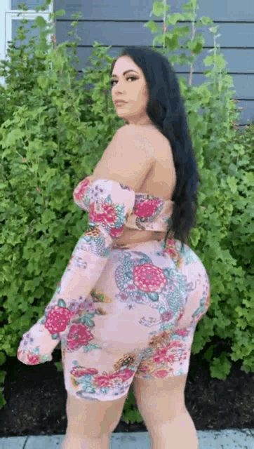 a woman is standing in front of a bush wearing a pink dress .