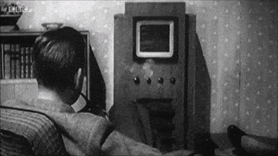 a black and white photo of a man sitting in front of a television