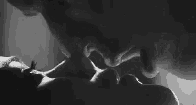 a black and white photo of a man and a woman kissing .