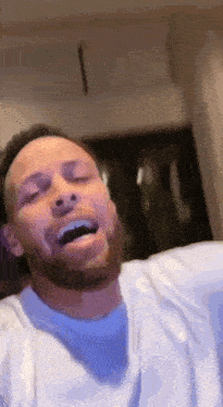a man with a beard and a white shirt is laughing with his eyes closed .