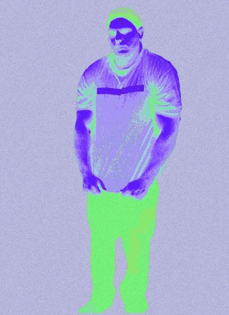 a man in a purple shirt and green pants stands in front of a gray background