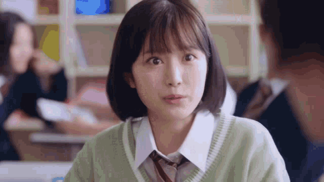 a girl in a school uniform is sitting at a desk in a classroom with other students .