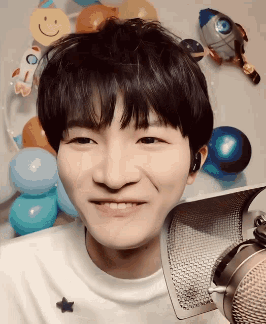 a young man is smiling in front of a microphone in front of balloons
