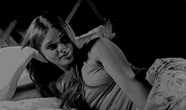 a black and white photo of a woman laying on a bed with her head on a pillow .