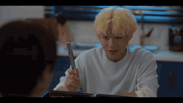 a man with blonde hair is holding a pair of tongs in his hand