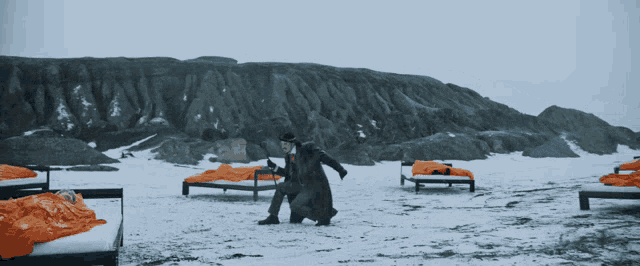 a man in a suit and hat is standing in the snow near a bed
