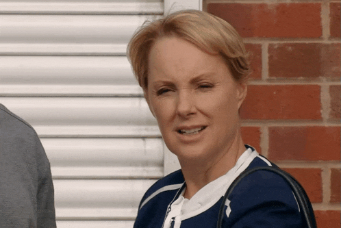 a woman wearing a blue jacket stands in front of a red brick wall