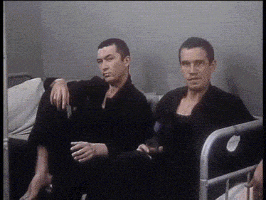two men are sitting on a couch and one is holding a glass