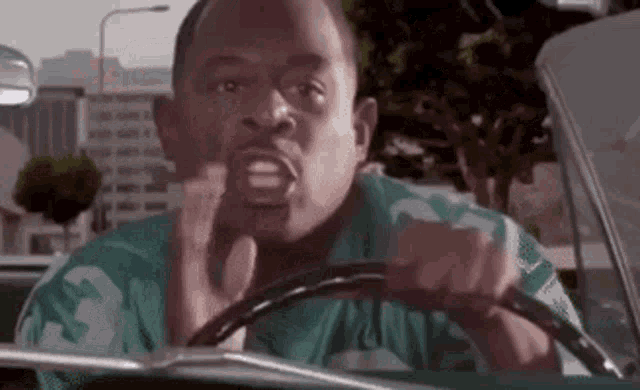 a man in a green shirt is driving a car and making a face .