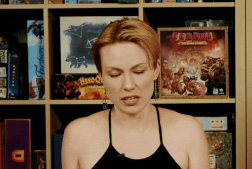 a woman stands in front of a shelf of board games including guardian