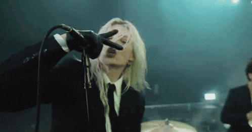 a woman singing into a microphone while wearing a black suit and tie